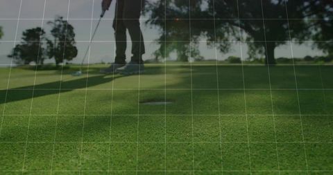Golfer Lining Up Putt on Sunlit Putting Green Near Hole with Long Shadow