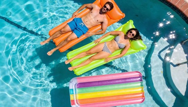 Young couple relaxing on orange and lime inflatable floats in sunlit backyard pool