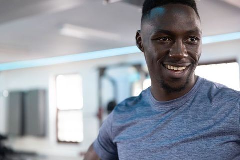 Confident african american man smiling in gym wearing blue athletic t-shirt