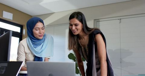 Indian colleagues collaborating over laptop wearing hijab and bindi in modern office team