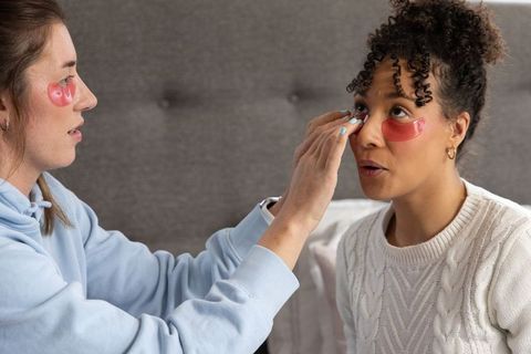 Multiracial friends applying pink hydrogel under-eye patches during cozy skincare session