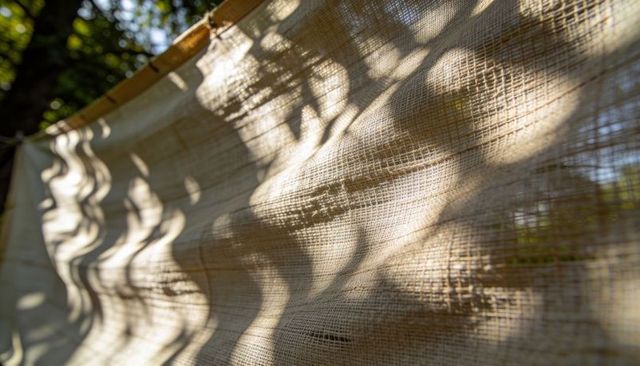 Draping beige woven sunshade casting dappled leaf shadows revealing fabric texture