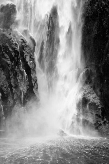 Majestic waterfall cascading down rocky cliffs with mist creating a mystical atmosphere. Perfect for posters, backgrounds, and designs related to nature's power, mystery, and tranquility.