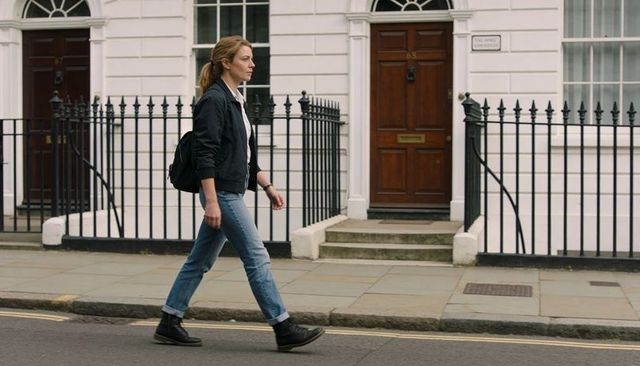 Walking woman carrying black backpack in bomber jacket and jeans on urban terraced street
