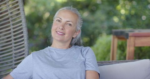 Smiling mature woman relaxing in wicker hanging chair on sunny patio