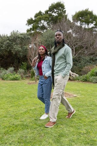 African american couple walking through lush garden wearing casual denim and scarves on overcast day