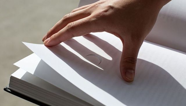 Hand turning page with crescent cutout casting sharp shadow on hardcover book