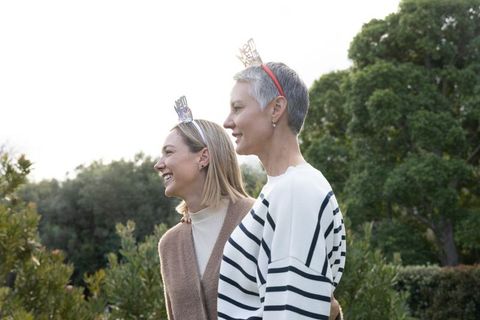 Mature women laughing and embracing in garden wearing metallic crown headbands