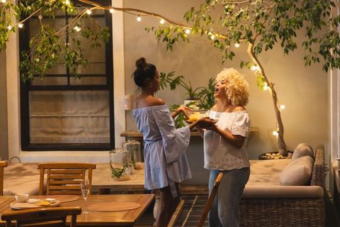 Two women sharing platter on cozy evening patio under string lights, casual hospitality