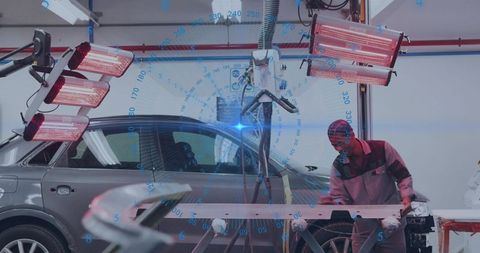 Technician aligning car bumper with infrared curing lamps in automotive bodyshop