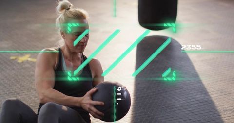 Blonde athlete performing medicine ball core workout beside heavy bag with ar overlay