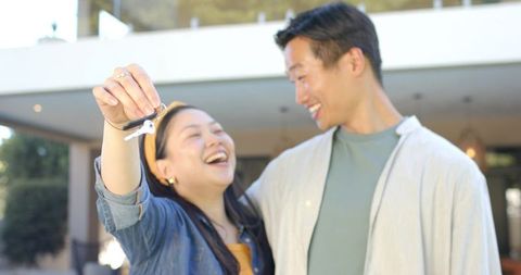 Young asian couple celebrating new home holding keys and sharing joyful embrace