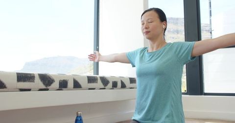 Woman practicing mindful stretching and meditation by sunlit window with mountain view