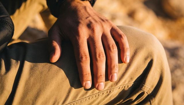Resting male right hand on khaki thigh at golden hour closeup wristband shadow detail