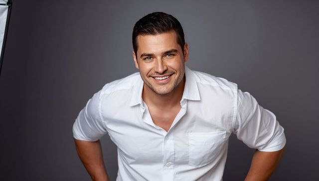Confident smiling man leaning forward in crisp white shirt studio headshot
