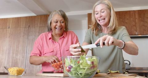 Female Friends Making Fresh Salad Together in Home Kitchen