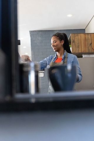 Smiling african american barista preparing espresso behind rustic cafe counter with milk jug