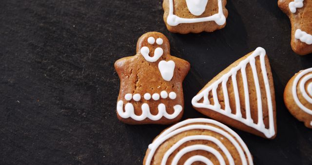 Gingerbread cookies with white icing designs are presented on a dark surface, offering a festive and sweet treat. Their intricate decorations suggest a holiday theme, often associated with Christmas or winter celebrations.