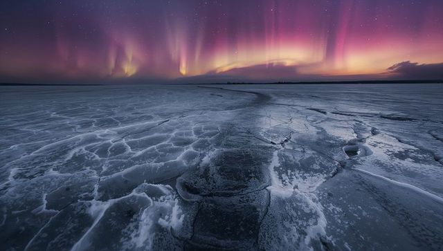 Aurora borealis over cracked frozen lake with curving ice channel and starry night sky