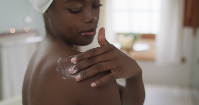 A woman demonstrating a self-care routine by applying lotion to her shoulder. This image can be used for wellness blogs, skincare product advertisements, beauty magazines, or health and wellness materials. It highlights themes of pampering, self-care, and relaxation.