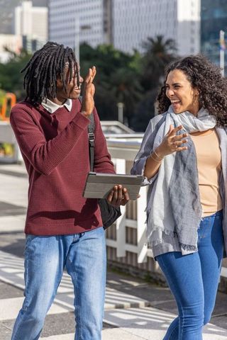 Friends walking and laughing on urban bridge holding tablet with highrise skyline