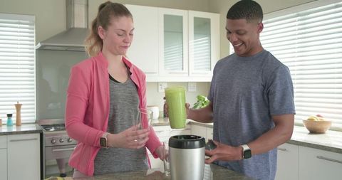 Couple making green smoothie in sunlit modern kitchen for healthy lifestyle and meal prep
