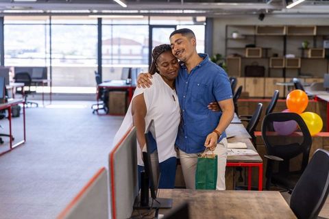 Diverse coworkers hugging in modern workspace together joyful