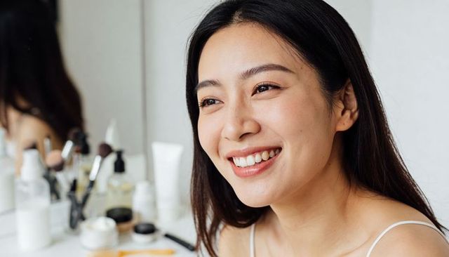 Smiling asian woman at vanity touching face natural skincare routine morning glow