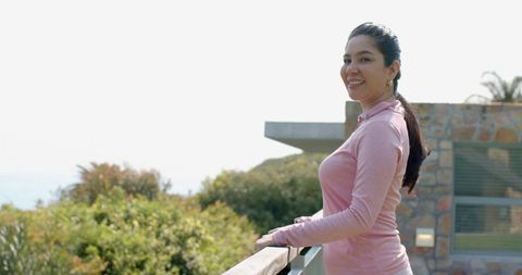 Smiling woman enjoying coastal balcony view in pink top, modern veranda lifestyle