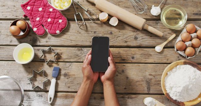 Image of hands of woman holding smartphone with copy space over baking ingredients and tools. baking, food preparing, taste and flavour concept.