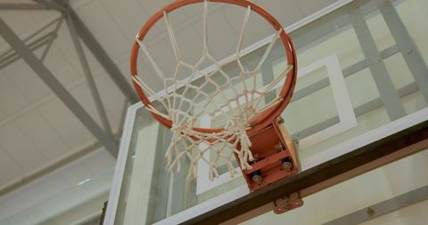 Low-angle showing basketball hoop and glass backboard with gym trusses and mounting bracket