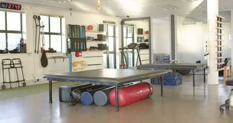 Spacious rehabilitation center gym featuring various equipment designed for physical therapy and rehabilitation. The area includes exercise and mobility aids, emphasizing a focus on recovery and healthcare. Ideal for promoting wellness, fitness programs, and rehabilitation services. Perfect for use in healthcare brochures, therapy session advertisements, or wellness-related articles.
