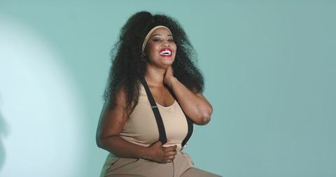 Confident african american woman smiling, wearing headband and suspenders in teal studio
