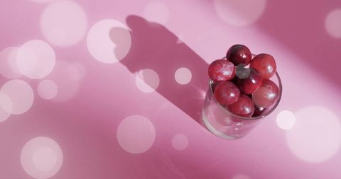 Red Grapes in Glass on Pink Background with Light Bokeh