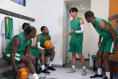 Basketball team discussing strategy in locker room holding basketballs in green uniforms