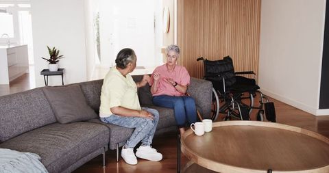 Happy senior lesbian couple talking at home with wheelchair