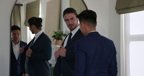 Groom Getting Ready in Front of Mirror with Friend Assisting