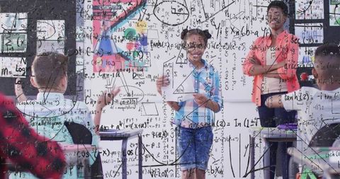 Girl presenting math in classroom wearing light blue top and denim shorts with formulas overlay