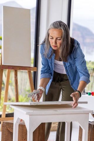 Mature woman preparing canvas with palette knife in bright studio overlooking mountains