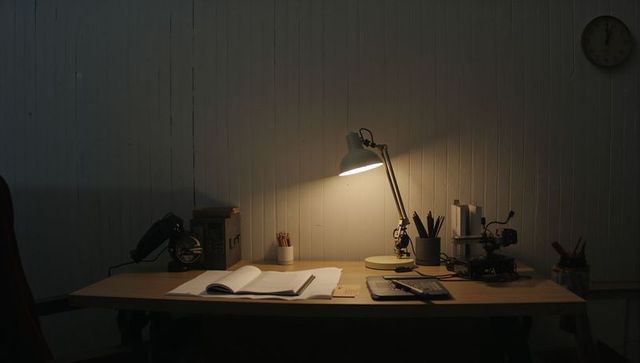 Moody desk lamp illuminating vintage wooden workspace with open notebook and rotary phone