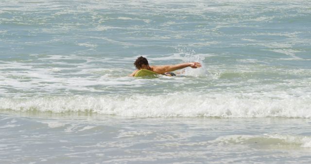 This image shows a man surfing in the ocean waves on a sunny day. Ideal for use in materials promoting water sports, adventure activities, beach vacations, and summer fun. The dynamic action and natural setting highlight a love for the sea and active lifestyle.