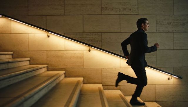 Businessman running up stone staircase in modern lobby with warm backlit handrail