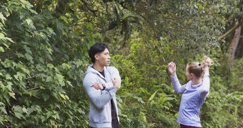 Outdoor fitness couple pausing on forest trail checking smartwatch and tying hair together