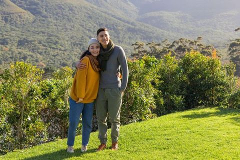 Asian couple embracing on hillside lookout wearing cozy sweaters and scarves