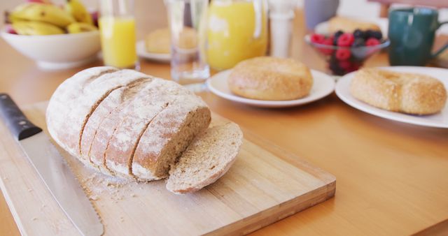 Freshly sliced bread on wooden cutting board next to a knife. Ideal for breakfast themes, dietary and nutrition articles, healthy lifestyle blogs. Additionally, it captures the cozy and inviting atmosphere of a morning meal, suitable for kitchen and food photography collections.
