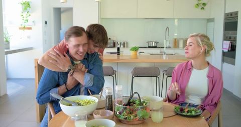 Young friends hugging and sharing pasta at bright modern kitchen island