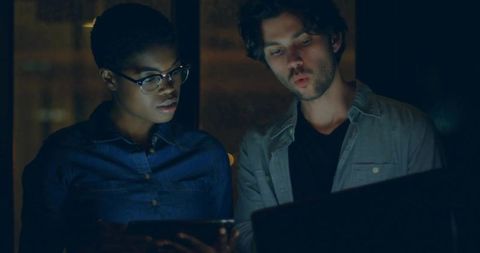 Two colleagues collaborating over laptop and tablet in low light coworking at night