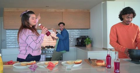 Multicultural friends dancing and cooking at modern kitchen island with colorful drinks