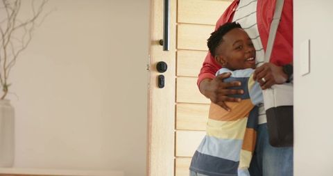 African american father hugging son at home entryway by wooden door, warm greeting