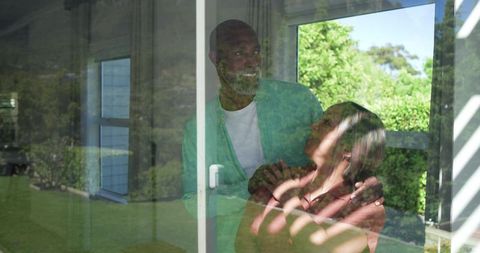 Sunlit diverse couple sharing tender embrace by sliding glass door with blinds shadows